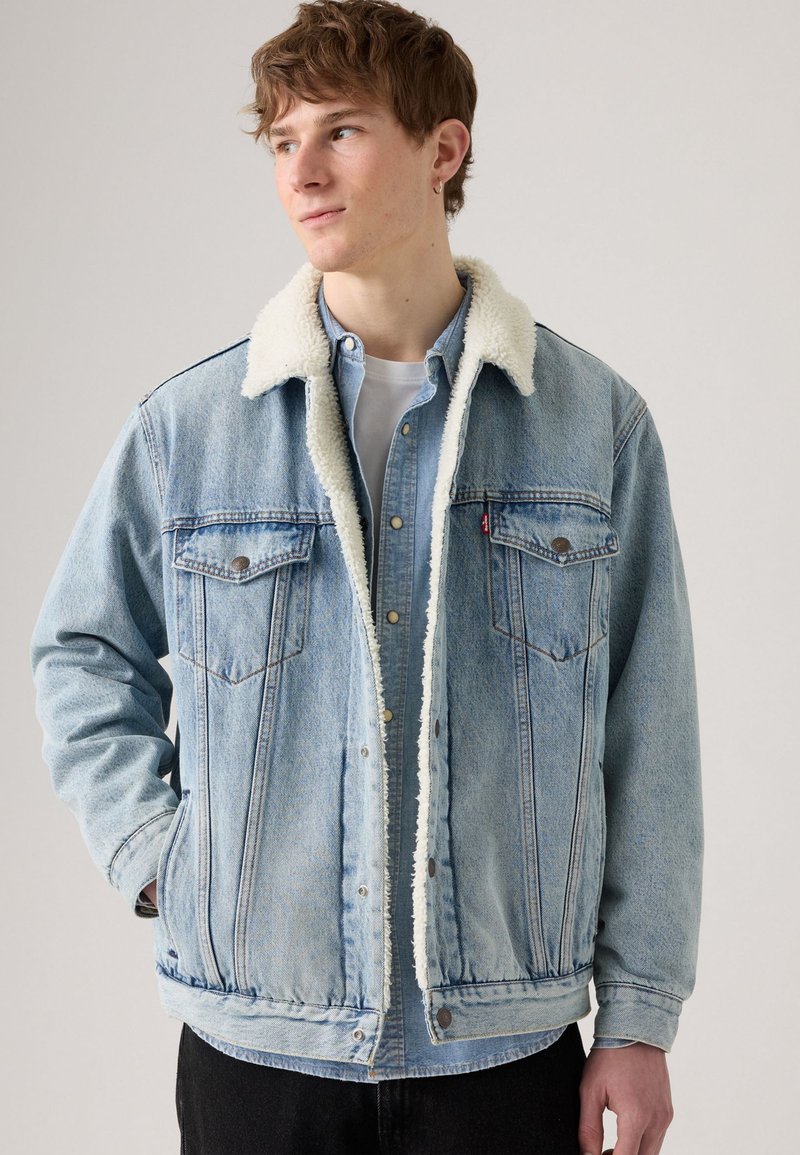 Light blue denim jacket with a white faux shearling collar, two chest pockets, snap buttons, and a relaxed fit. Textured fabric appears worn.