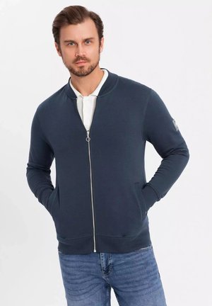 Sudadera con cremallera en color navy, hecha de una tela suave, con puños y dobladillo acanalados, bolsillos laterales y un pequeño parche con logotipo en la manga.