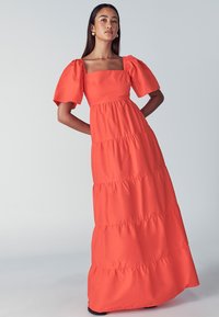 Korallenfarbenes Maxikleid mit Puffärmeln, quadratischem Ausschnitt und gestufter Volantgestaltung. Hergestellt aus leichtem Stoff mit glatter Textur.