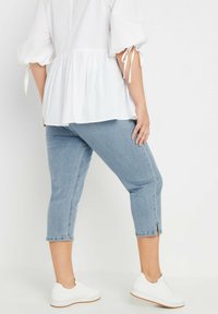 Valkoinen peplum-toppi puffatuilla hihoilla ja solmukoilla, yhdistettynä vaaleansinisiin lyhyisiin farkkuihin, joissa on sivuleikkaukset, täydentäen asua valkoisilla lenkkareilla.