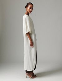 Μακρύ, ρέον φόρεμα από απαλό λευκό ύφασμα με κοντά μανίκια. Διακριτικές πλευρικές σκισμές και συνδυάζεται με ψηλοτάκουνα σανδάλια με λουράκια. Απλός, κομψός σχεδιασμός.