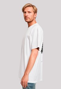 White cotton T-shirt featuring a black graphic design on the back, loose fit, short sleeves, and a round neckline.
