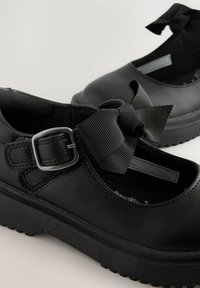 Zapatos de imitación cuero negros con un acabado texturizado, que presentan una punta cuadrada, suela de goma gruesa y un lazo de cinta negro acentuado con una hebilla de metal.