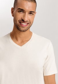 Tričko s výstřihem do V v měkké smetanové látce; krátké rukávy, hladká textura, minimalistický design bez vzorů nebo akcentů.