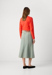 Rød ullgenser, kort med lange ermer, kombinert med et lys blå denim midi-skjørt med sidesømmer og rett passform. Sorte leiligheter.