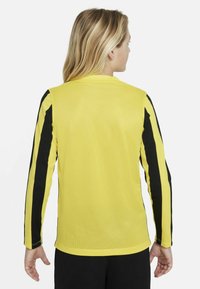 Maglia a maniche lunghe in tessuto a rete giallo brillante, con strisce laterali nere e scollo rotondo. Texture liscia con vestibilità atletica.