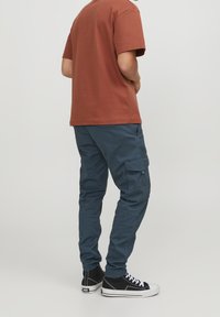 Brun kortärmad t-shirt i kombination med blå cargobyxor med fickor och elastiska muddarna, kompletterad med svarta högskaftade sneakers.