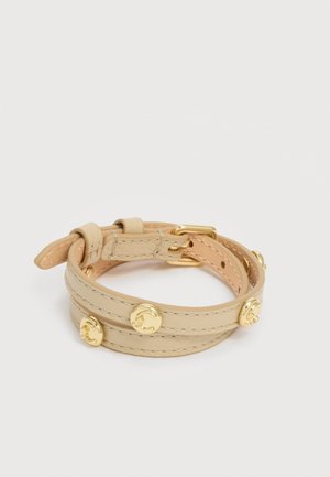 Βραχιόλι περιτύλιξης από μπεζ δέρμα με αγκράφα σε χρυσό τόνο και στρογγυλές διακοσμητικές στρας, απλωμένο επίπεδα σε λευκό φόντο.