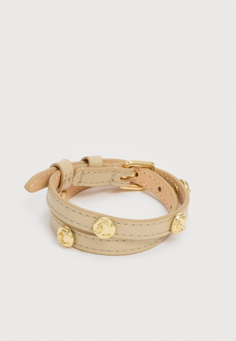 Βραχιόλι περιτύλιξης από μπεζ δέρμα με αγκράφα σε χρυσό τόνο και στρογγυλές διακοσμητικές στρας, απλωμένο επίπεδα σε λευκό φόντο.
