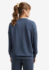 Dunkelblaues Sweatshirt aus weichem Stoff, mit lockerer Passform, abfallenden Schultern und gerippten Bündchen. Glatte Textur mit minimaler Detailgestaltung.