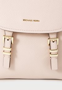 Lichtroze, gestructureerde leren rugzak met gouden hardware accenten en een klep met dubbele gesp-sluitingen. Het Michael Kors-logo is erop gedrukt.
