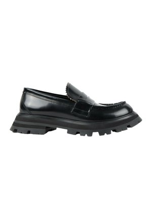 Mocassin en cuir noir avec une semelle épaisse à crampons et une large sangle sur le dessus, présenté de la face extérieure sur fond blanc.