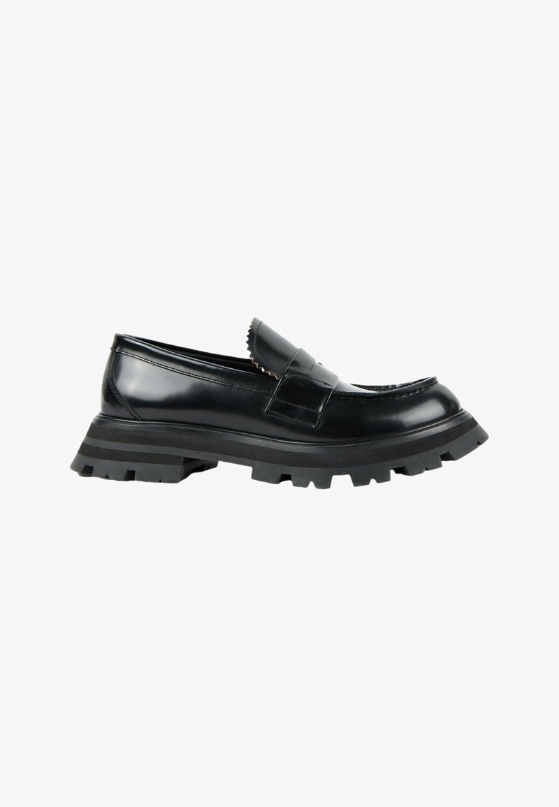 Mocassin en cuir noir avec une semelle épaisse à crampons et une large sangle sur le dessus, présenté de la face extérieure sur fond blanc.