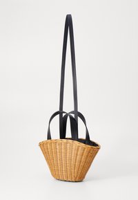 Tkaná slámová taška s zužujícím se tvarem, přírodní barvou a černými koženými uchy. Vyznačuje se texturovaným povrchem a otevřeným vrchem.