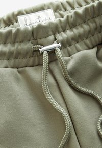 Ljusgröna dragstringbyxor med en texturerad tyg, elastisk midja och metalliska detaljer. Förstärkt sömnad längs kanterna.