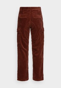 Bruine corduroy broek met rechte pijpen, achterzakken met klep en zijcargo zakken, van achteren getoond op een eenvoudige witte achtergrond.