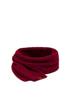 Femme portant une écharpe tricotée rouge foncé assortie, des gants sans doigts et des chauffe-bras sur un haut noir à manches longues avec des mèches de cheveux lâches.