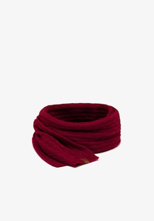 Femme portant une écharpe tricotée rouge foncé assortie, des gants sans doigts et des chauffe-bras sur un haut noir à manches longues avec des mèches de cheveux lâches.