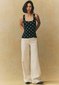 Black polka dot tank top with square neckline paired with beige wide-leg trousers. Smooth fabric, minimal details, and pointed black shoes.
