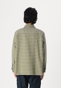 Kontrollerad grön och beige flanellskjorta med långa ärmar, knäppning vid manschetterna och klassisk krage; har en något sänkt nederdel bak.