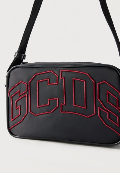 Μαύρη ορθογώνια τσάντα ώμου με ρυθμιζόμενο ιμάντα και μεγάλα κόκκινα γράμματα με περίγραμμα "GCDS" μπροστά.