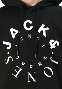 Must küll hoody suure valge graafikuga, millel on tekst "JACK" ja "Jones", kasutades erinevaid fondi suurusi ja orientatsioone ning tõmblukke.