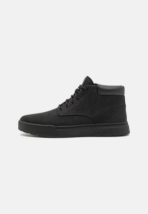 Czarny wysokiej jakości sneaker z sznurowaniem z przodu, wyściełanym kołnierzem i teksturowaną podeszwą, pokazany w profilu na jasnym, jednolitym tle.