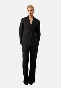 Zwarte krijtstreep pak met een dubbelzijdig jasje en op maat gemaakte broek. Glad materiaal, scherpe revers en minimalistische knopen.