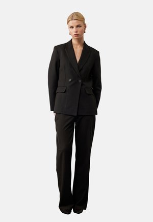 Costume noir à rayures, comprenant une veste croisée et un pantalon taillé. Tissu lisse, revers pointus et boutons minimalistes.
