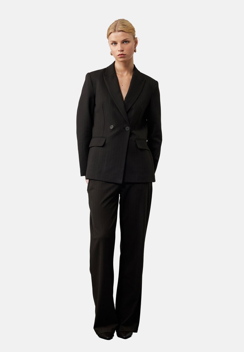 Zwarte krijtstreep pak met een dubbelzijdig jasje en op maat gemaakte broek. Glad materiaal, scherpe revers en minimalistische knopen.