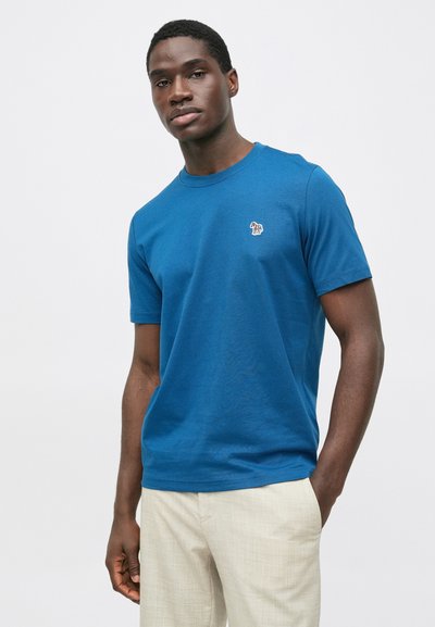 Niebieska bawełniana koszulka z krótkimi rękawami, okrągłym dekoltem i małym wielokolorowym haftowanym logo na piersi. Gładka struktura.