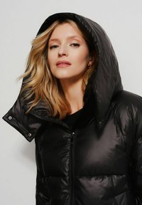 Czarna puchowa kurtka z wysokim kołnierzem i dużym kapturem. Gładki, błyszczący materiał z pikowanymi sekcjami oraz frontowym zapięciem na zamek.