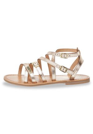 Sandalettes à lanières en rose gold métallisé avec plusieurs lanières et accents de boucles. Semelle plate, design à bout ouvert et finition en cuir texturé.