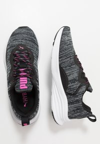Chaussures de sport en tricot noires et grises avec des accents et des lacets roses, dotées d'une semelle intermédiaire blanche et d'une semelle extérieure en caoutchouc texturé.