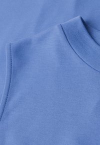 Gros plan d'un sweat-shirt bleu clair plié montrant le col rond bord-côte et la couture de l'épaule en tissu de coton doux.