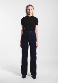 Černé tričko s krátkým rukávem a tmavě modré džíny s vysokým pasem. Džíny mají rovný střih nohavic a minimální množství švů.