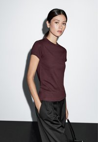 Bordeaux heren tee met korte mouwen, ronde hals, gladde textuur, gecombineerd met zwarte losse broek. Eenvoudig en modern ontwerp.