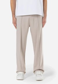 Beige bukser lavet af blødt stof, med en afslappet pasform, frontfolder og lige ben, parret med hvide sneakers.