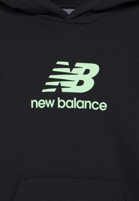 Juoda hoodie su šviesiai žaliu New Balance logotipu ir prekinio pavadinimo užrašu, centruotu virš priekinės kišenės.