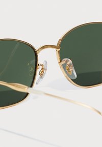 Gold metal sunglasses with green lenses, rectangular shape, clear nose pads, and thin, elegant arms. Notable for minimalistic design.