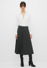Blusa bianca con zip frontale, abbinata a una gonna grigia scuro a righe verticali di lunghezza al ginocchio. La modella indossa stivali neri con tacco alto. Design semplice e strutturato.