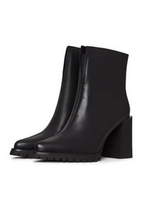 Paire de bottines noires en cuir avec des talons blocs épais et des semelles en caoutchouc rainurées, présentées côte à côte sur un fond blanc.