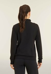 Felpa nera con colletto alto, maniche lunghe e polsini a costine. Realizzata in materiale morbido con una texture liscia, dettagli di cucitura minimi.