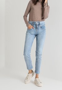 Světle modré džínové kalhoty s taperovaným střihem, vysokým pasem a pěti kapsami, zkombinované s hnědým pruhovaným dlouhým rukávem a béžovými teniskami.