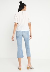 Biała, fakturowana bluzka z krótkimi bufiastymi rękawami i rozcięciem z tyłu. Połączona z jasnoniebieskimi dzwonami i wzorzystymi klapkami na obcasie.