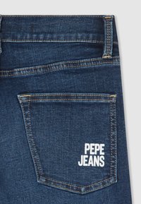 Tmavomodré džínové kalhoty s zadní kapsou, na které je bílý nápis "PEPE JEANS", kontrastní šití a texturovaný povrch látky.