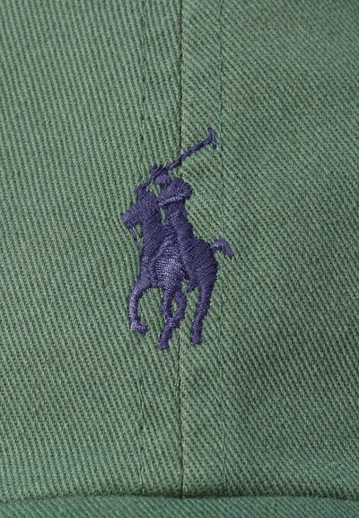 Zaļš beisbola cepure, izgatavota no teksturēta auduma, ar izteiktu tumši zilu izšuvumu polo spēlētāja logo priekšpusē.