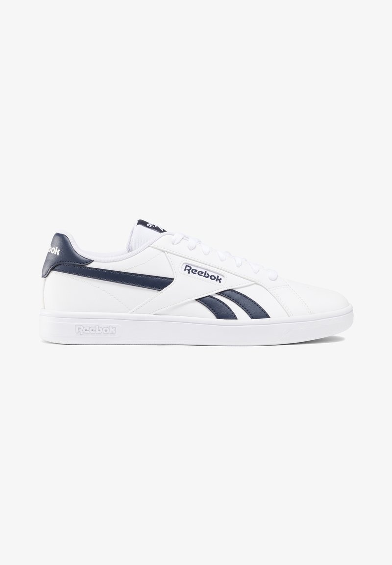 Baskets basses blanches Reebok avec des bandes latérales bleu marine, logo sur le côté et le talon, et lacets blancs sur fond blanc.