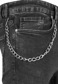 Jeans de mezclilla negra con un accesorio de cadena plateada adjunto en la cinturilla, que presenta un diseño de eslabones y un detalle de remache encima del bolsillo.