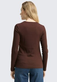 Braunes Langarmoberteil mit rundem Ausschnitt und weichem, strukturiertem Stoff. Die Rückseite hat ein einfaches Design und wird mit blauen Jeans kombiniert.